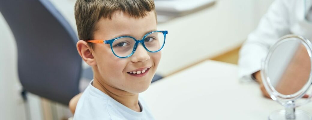 En la fotografía se aprecia un niño sonriente con gafas azules sentado en una consulta oftalmológica, simbolizando la importancia del control de la vista en la infancia.